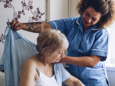 Caregiver helping elderly woman to put on clothes