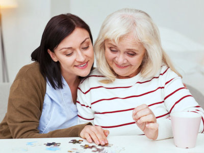 Caregiver together with elderly woman completing jigsaw puzzle