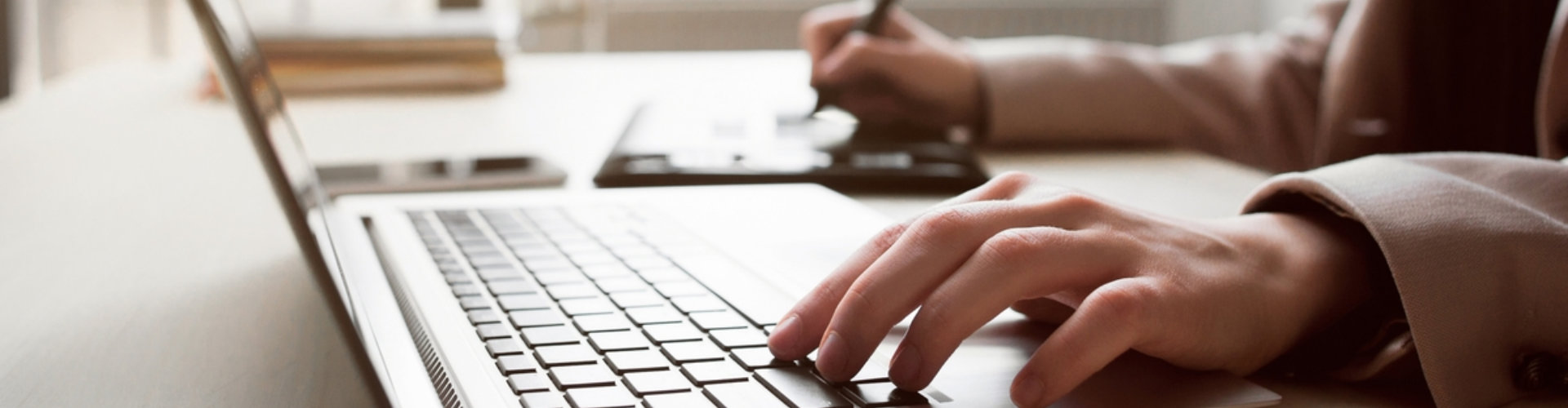 Person using laptop while writing on the other hand