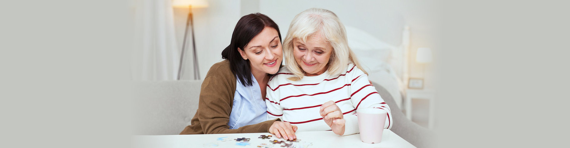 Caregiver together with elderly woman completing jigsaw puzzle